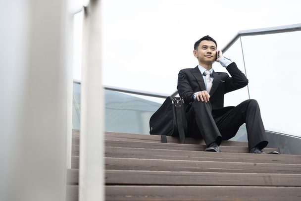 handsome business man speaking mobile phone sitting in the stair - Foto, imagen