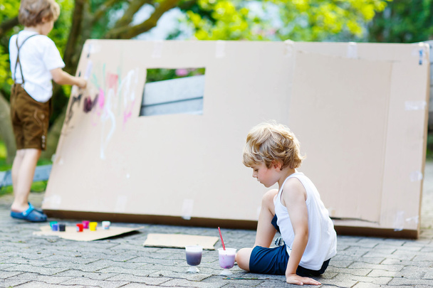 Two little kid boys painting big paper house with colorful paint - 写真・画像