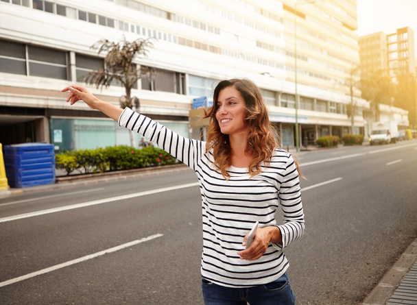 Cheerful young woman hailing a cab on city street - Fotoğraf, Görsel