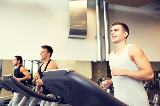 улыбающиеся мужчины тренируются на беговой дорожке в тренажерном зале
 - Фото, изображение
