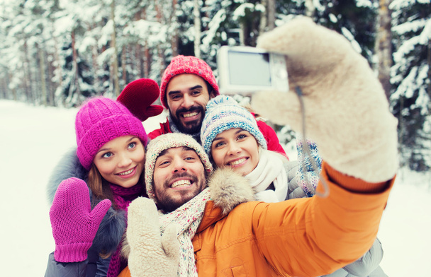 smiling friends with camera in winter forest - Zdjęcie, obraz