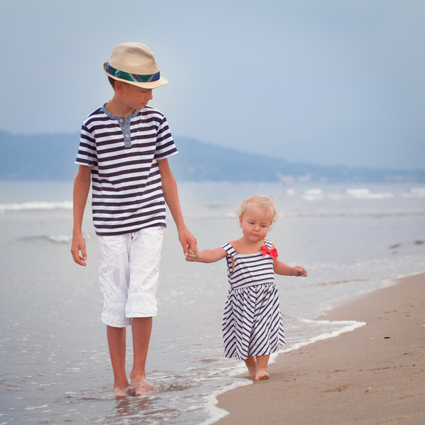 glücklicher älterer Bruder und jüngere süße Schwester, die an der Küste spazieren gehen - Foto, Bild