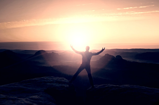 Jumping hiker in black celebrate triumph between two rocky peaks. Wonderful daybreak with sun above head.. - Photo, Image