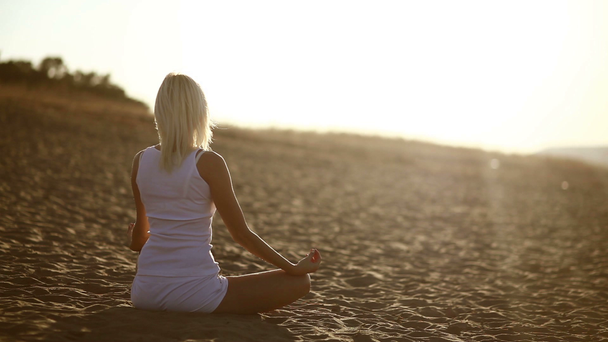 žena v bílé seděl na písku meditace zdravého životního stylu západu slunce zapadne, siluetu proti obloze jóga - Záběry, video