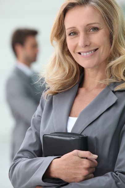 Smiling businesswoman holding personal organiser with colleague in backgrou - Photo, Image