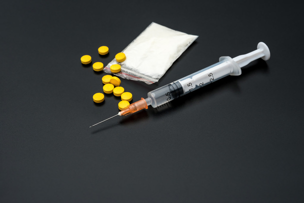 Jednorazowe strzykawki i opakowanie białego proszku i tabletki na czarnym tle - Zdjęcie, obraz