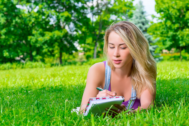 attractive young woman making notes in a notebook lying on the g - Photo, Image