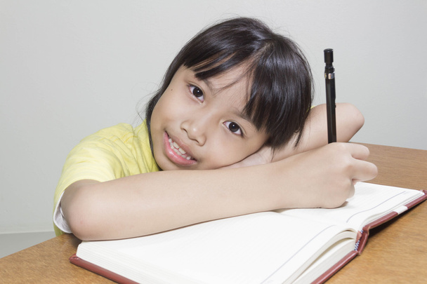Азіатські дівчата дитина щасливий працювати в залі, сидять її пером у руці писати нотатки книга білого паперу - Фото, зображення