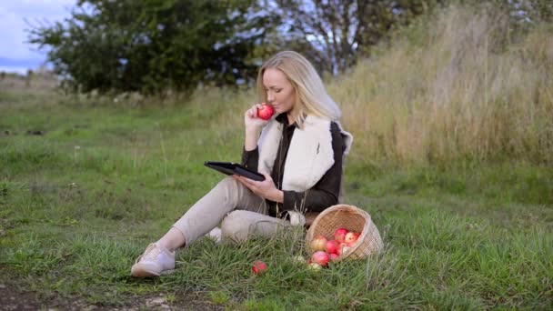 Young woman holding in one hand apple, in the other hand tablet - Кадри, відео