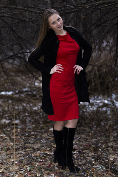 girl in red dress and black coat standing in winter park - Foto, Bild