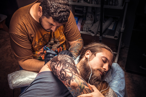 Άνθρωπος φορώντας τα γάντια κάνει δροσερό τατουάζ στην αίθουσα δερματοστιξιών - Φωτογραφία, εικόνα