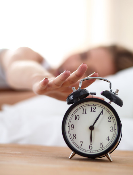 Young sleeping woman and alarm clock in bedroom at home - Fotó, kép