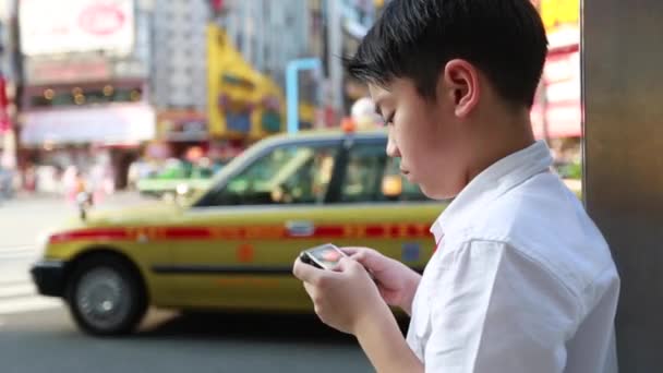 Szczęśliwy chłopiec azjatyckich przy użyciu inteligentnych telefonów w pobliżu ulicy walking street w Tokyo, Japonia - Materiał filmowy, wideo