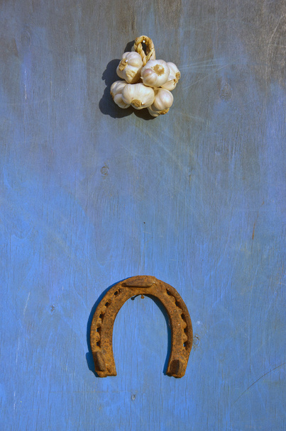 Mazzo di aglio e ferro di cavallo illuminato dal sole su sfondo blu
 - Foto, immagini