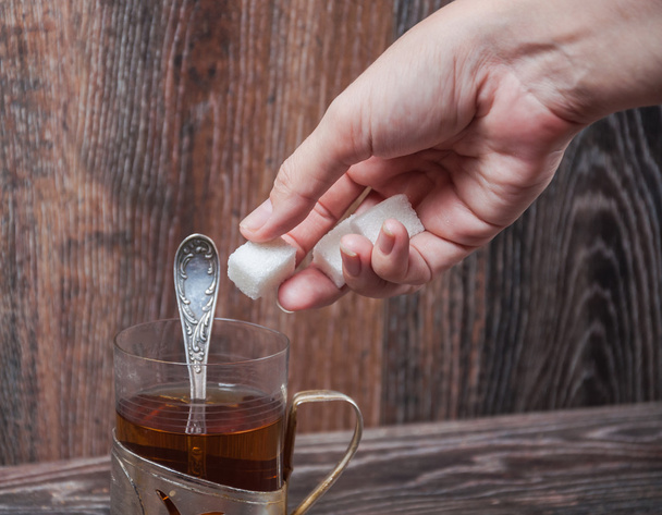 Το χέρι που ρίχνει ένα κομμάτι της ζάχαρης σε ένα ποτήρι του τσαγιού - Φωτογραφία, εικόνα