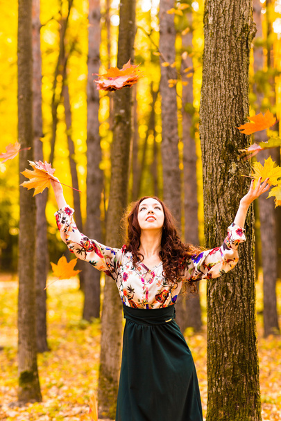 Jonge mooie vrouw gooien gele bladeren in de lucht - Foto, afbeelding