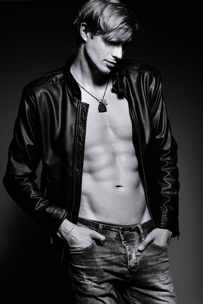 Young handsome muscled fit male model man in leather jacket posing in studio showing his abdominal muscles - Foto, afbeelding