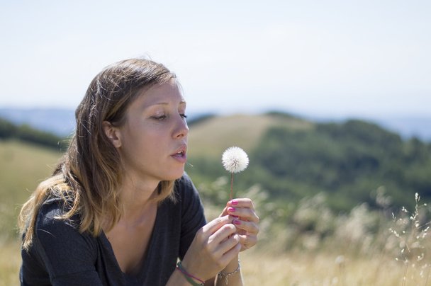 Brunette girl blowing a dandelion in the field - Photo, Image