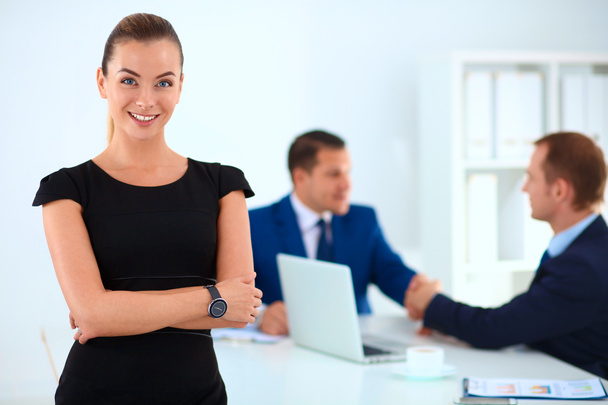 Portrait of a beautiful businesswoman standing in an office with colleagues shaking hands in the background - Photo, Image