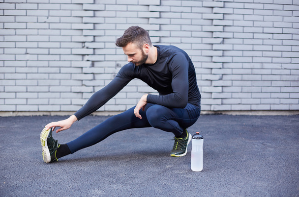 Sportovní muž s plnovousem, táhnoucí se proti betonové zdi - Fotografie, Obrázek