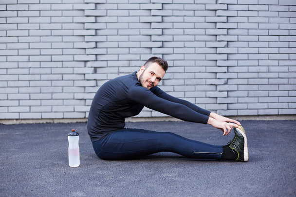 Sport man with beard stretching against concrete wall - 写真・画像