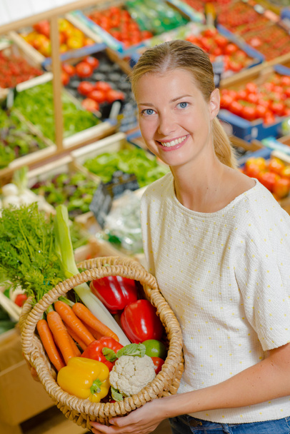 Woman holding up a basket of vegetables - Foto, afbeelding