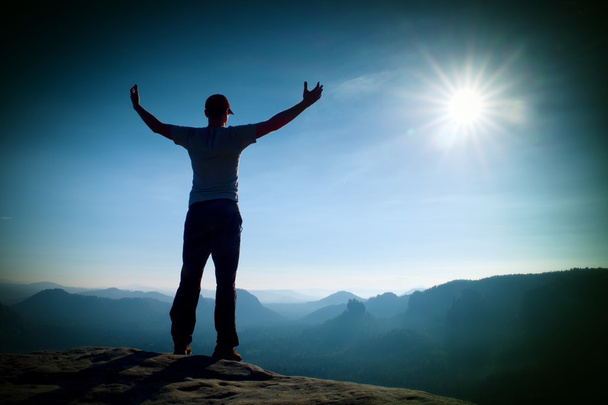 Felice gesto dell'uomo in berretto rosso di trionfo con le mani in alto. Divertente escursionista sulla cima della roccia arenaria nel parco della Sassonia Svizzera
 - Foto, immagini