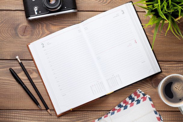 Schreibtisch mit Kalender-Notizblock, Kamera, Zubehör und Blumen - Foto, Bild