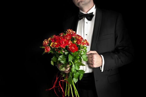 Κομψό άνδρας στο σμόκιν κρατώντας κόκκινα τριαντάφυλλα - Φωτογραφία, εικόνα
