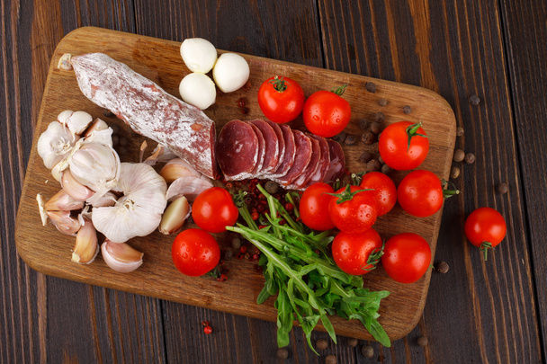 Salami with cherry tomatoes, ruccola and garlic on a cutting boa - Foto, afbeelding