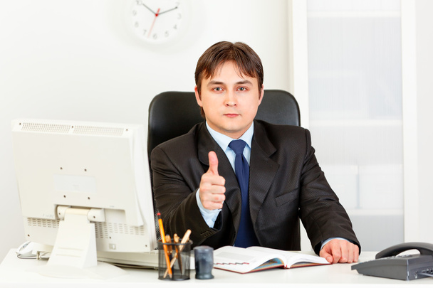 Confident modern businessman sitting at office desk and showing thumbs up g - Zdjęcie, obraz