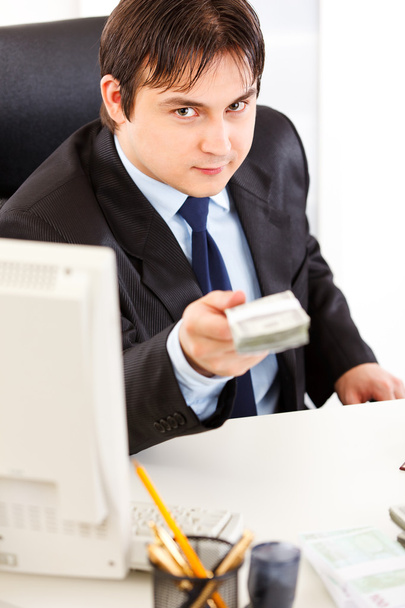 Smiling businessman sitting at office desk and giving dollars packs - Zdjęcie, obraz