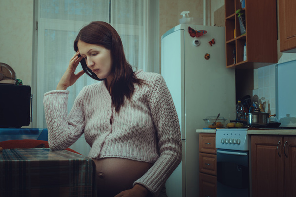 Θλιβερή έγκυος γυναίκα που κάθεται στην κουζίνα. - Φωτογραφία, εικόνα