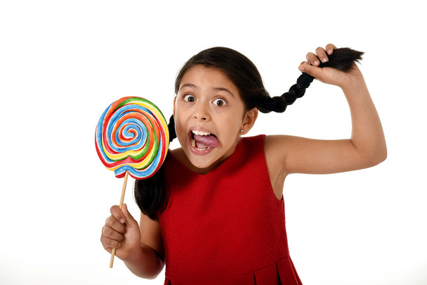 happy female child holding big lollipop candy pulling pony tail with crazy funny face expression in sugar addiction - Photo, Image