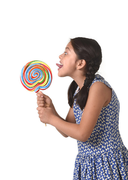 happy female child holding big lollipop candy licking the candy with her tongue in sugar addiction - Fotoğraf, Görsel