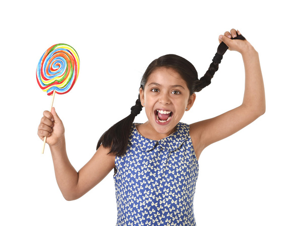 happy female child holding big lollipop candy pulling pony tail with crazy funny face expression in sugar addiction - Fotó, kép