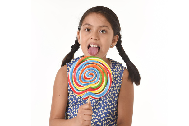 happy female child holding big lollipop candy licking the candy with her tongue in sugar addiction - Фото, изображение