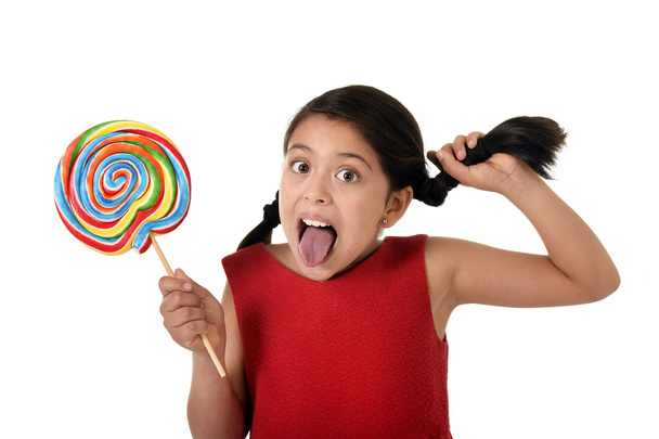 happy female child holding big lollipop candy pulling pony tail with crazy funny face expression in sugar addiction - Foto, afbeelding