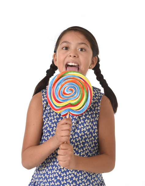happy female child holding big lollipop candy licking the candy with her tongue in sugar addiction - Fotó, kép