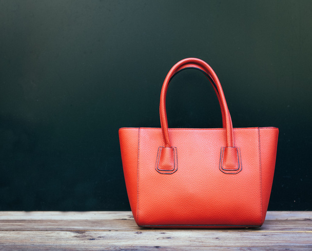 Fashionable beautiful big red handbag standing on a wooden floor on black wall background. Still life. Warm color - Foto, imagen