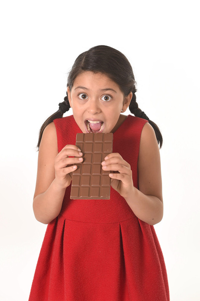 glückliche weibliche Mädchen in rotem Kleid mit beiden Händen große Schokolade essen in fröhlich aufgeregtem Gesichtsausdruck in zuckerhaltiger Ernährung - Foto, Bild