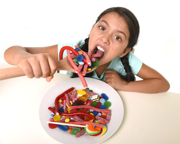 happy young girl holding spoon eating from dish full of candy lollipop and sugary things - Zdjęcie, obraz