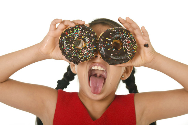 latin child in red dress playing with donuts in her hands putting them on her face as cake eyes - Photo, Image