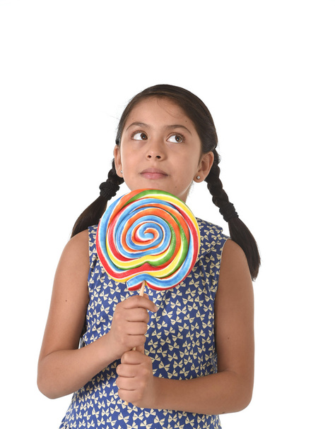Latin female child holding huge lollipop happy and excited in cute blue dress and pony tails candy concept - Fotoğraf, Görsel
