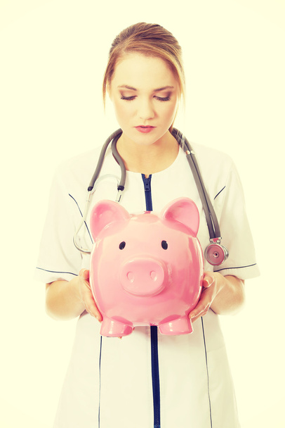 Young female doctor holding a piggybank. - Zdjęcie, obraz