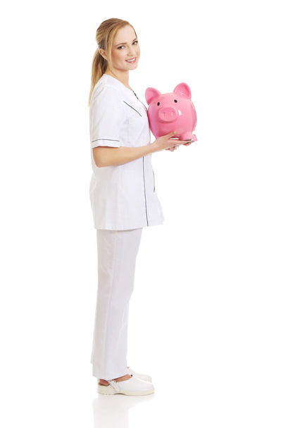Young female doctor holding a piggybank. - Valokuva, kuva