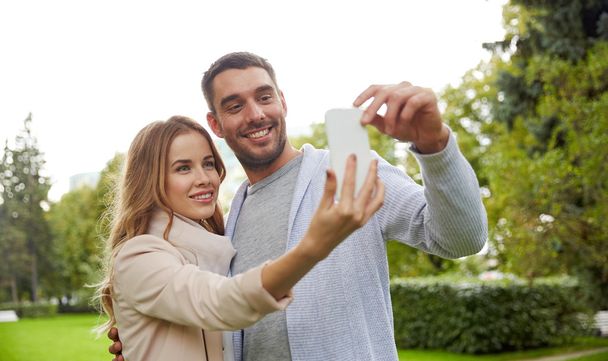 happy couple with smartphone taking selfie in park - Photo, Image