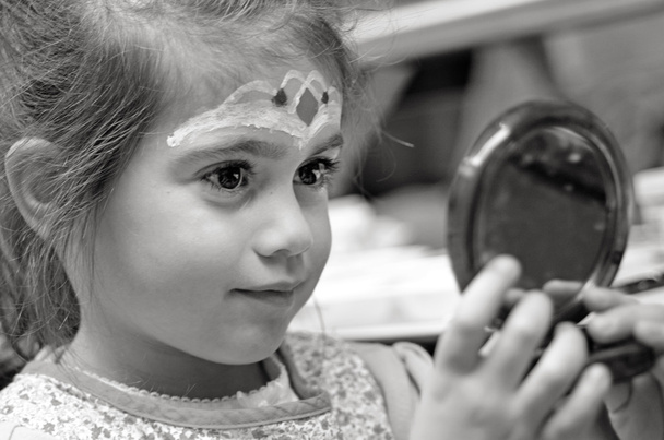 Little girl with face painting looks at the mirror - Фото, изображение