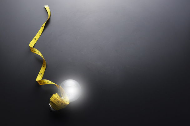 Lowlight sleutel van gloeilamp en geel meetlint met waterdruppel op grijze achtergrond - Foto, afbeelding
