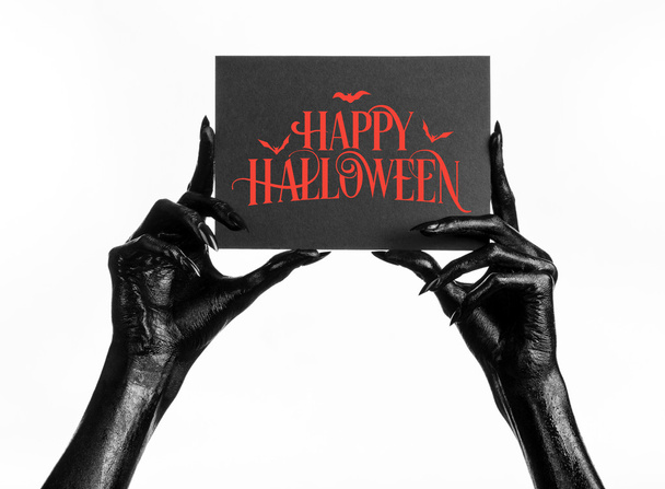 Postcard and Happy Halloween theme: black hand of death holding a paper card with the words Happy Halloween on a white isolated background in studio - Zdjęcie, obraz